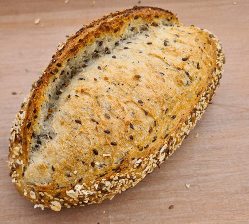 Artisan sourdough multigrain loaf with golden-brown crust, showing visible grains and seeds on rustic wooden cutting board